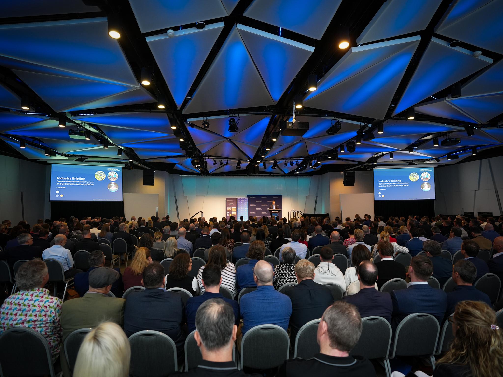 Crowded auditorium with screens at the front of the room that reads 'GIICA Industry Briefing Event'
